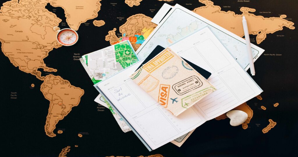 Travel documents, visa passport cover, and a notebook with 'Start the adventure' written on it, placed on a world map, representing UK student visa requirements and international study plans